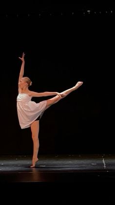 a young ballerina is performing on the stage with her arms in the air and one leg up