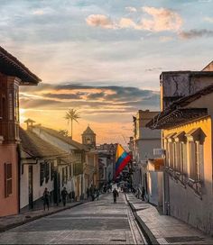 the sun is setting on an empty street with people walking down one side and buildings to the other