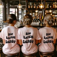 three women in pink shirts sitting at a bar with their backs turned to the camera