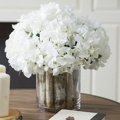 white flowers in a glass vase on a table next to a notepad and candles