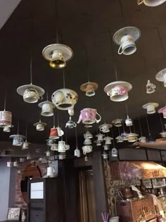 many cups and saucers hanging from the ceiling in a room with lights above them