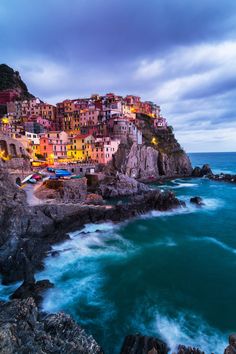 the colorful village is on top of a cliff by the ocean with waves crashing in front of it