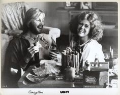 a man and woman sitting at a table with food in front of them, smiling