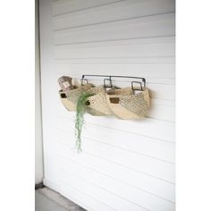 two baskets hanging on the side of a white building with plants growing out of them