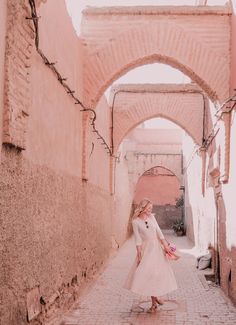 a woman in a white dress is walking through an alley way with arches and brick walls