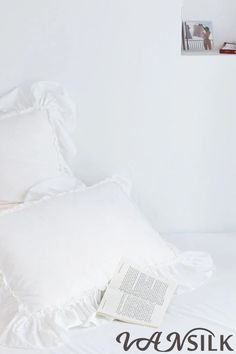 a white bed with two pillows and a book on the pillowcase next to it