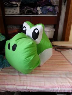 a green frog pillow sitting on top of a bed