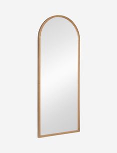 an arched wooden mirror on a white wall with a light brown frame and wood trim