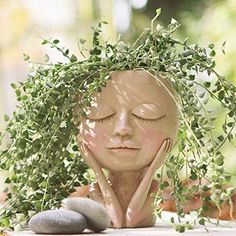 a clay head with eyes closed sitting next to some rocks and greenery on the table