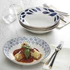 a white plate topped with pasta covered in sauce and garnished with green leaves