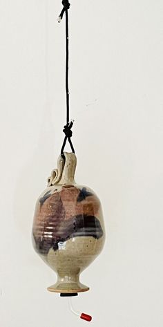 a ceramic vase hanging from a string with a small red object in the middle of it