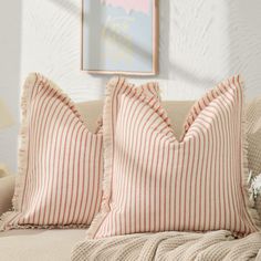 two red and white striped pillows sitting on top of a couch next to a painting