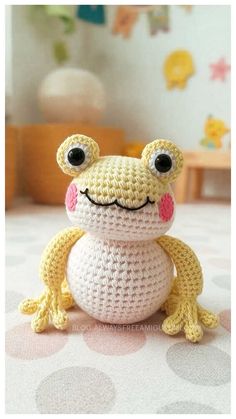 a crocheted frog sitting on top of a bed with its eyes wide open