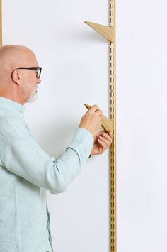 an older man is working on a wooden shelf with pegs and a ruler in front of him