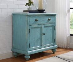 a blue cabinet with two drawers and a candle on top, in front of a white brick wall