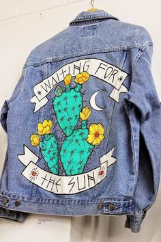 a denim jacket with an image of a cactus and flowers on it, hanging up against a wall