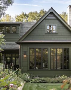 a green house with lots of windows on the front and side of it, surrounded by greenery