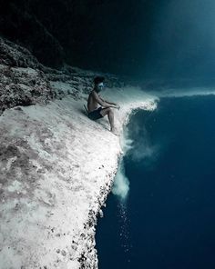 a man sitting on top of a cliff next to the ocean with his feet in the water