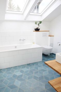 a bathroom with blue tile flooring and skylights above the bathtub, toilet and sink