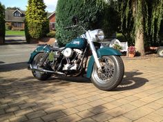 a blue motorcycle parked on the side of a brick road next to a green tree