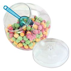 a glass bowl filled with lots of colorful candies next to a plastic container on top of a white surface