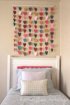 a bed with a white headboard topped with pillows and hearts hanging on the wall