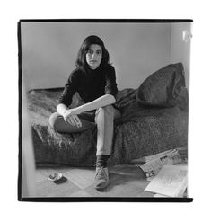 black and white photograph of a woman sitting on a bed with papers scattered around her