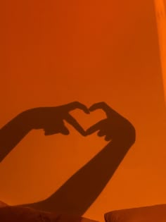 the shadow of two hands making a heart shape in front of an orange wall with pillows