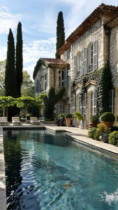 an outdoor swimming pool in front of a large house with trees and bushes around it