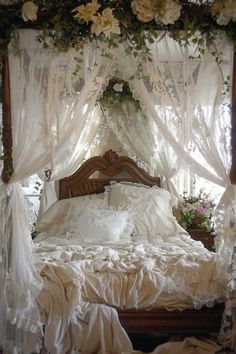 a bed with white sheets and flowers on the headboard is surrounded by sheer curtains