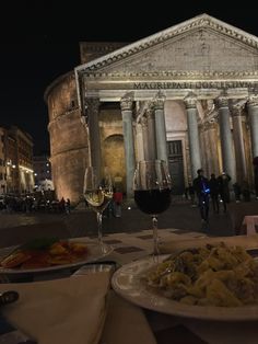 two plates of food and glasses of wine on a table in front of an old building