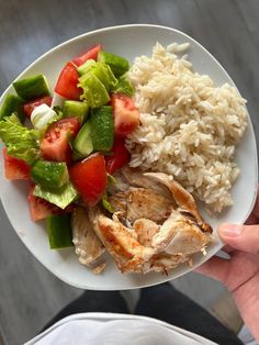 a person holding a plate with chicken, rice and vegetables