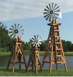 three wooden windmills sitting on top of a lush green field next to a lake