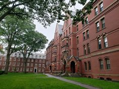 an old red brick building with many windows and trees in the foreground, on a cloudy day