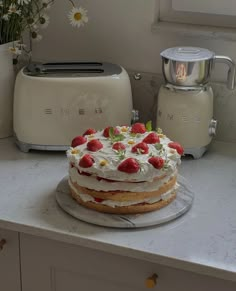 a cake sitting on top of a kitchen counter next to toaster ovens and flowers