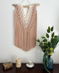 a wooden table topped with a vase filled with flowers and a crocheted wall hanging