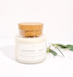 a candle with a cork lid sitting on a white surface next to a green plant