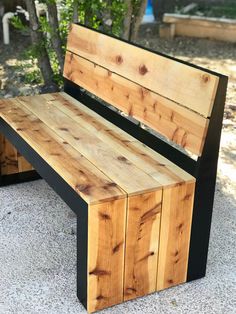 a wooden bench sitting on top of a cement ground next to a tree and bushes