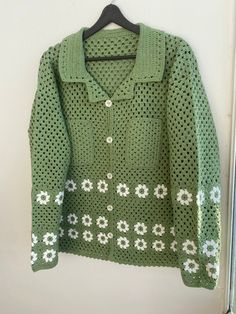 a green sweater with white flowers on it hanging from a hook in front of a wall