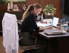 a woman sitting at a desk with a laptop computer on her lap and writing something