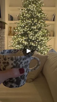 a person holding a coffee cup in front of a christmas tree with lights on it