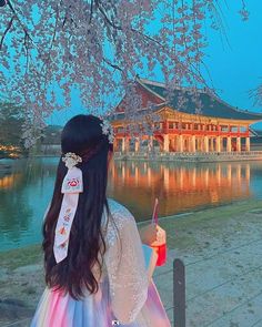 a woman standing under a cherry blossom tree next to a body of water with a building in the background