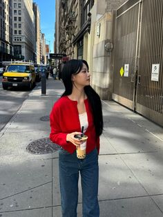 a woman standing on the sidewalk holding a drink and looking up at something in her hand