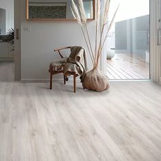 a living room with wooden floors and white walls is pictured in this image, there is a chair next to the door