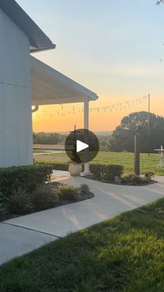 the sun is setting in front of a white house with lights strung from it's roof