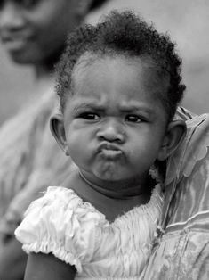 a black and white photo of a baby crying with her mother in the back ground