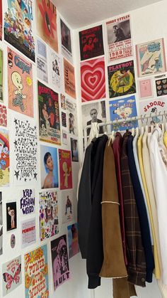 there is a wall covered with posters and t - shirts hanging on the clothes rack