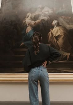 a woman standing in front of a painting looking at it's back with her hands on her hips