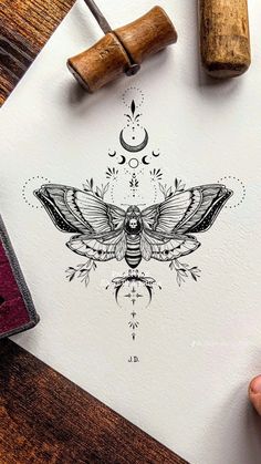 a drawing of a moth on paper next to a rubber stamp and some ink pens