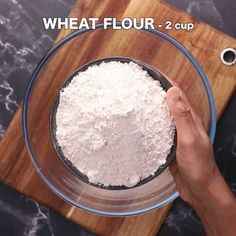 a person holding a bowl with flour in it on top of a wooden cutting board